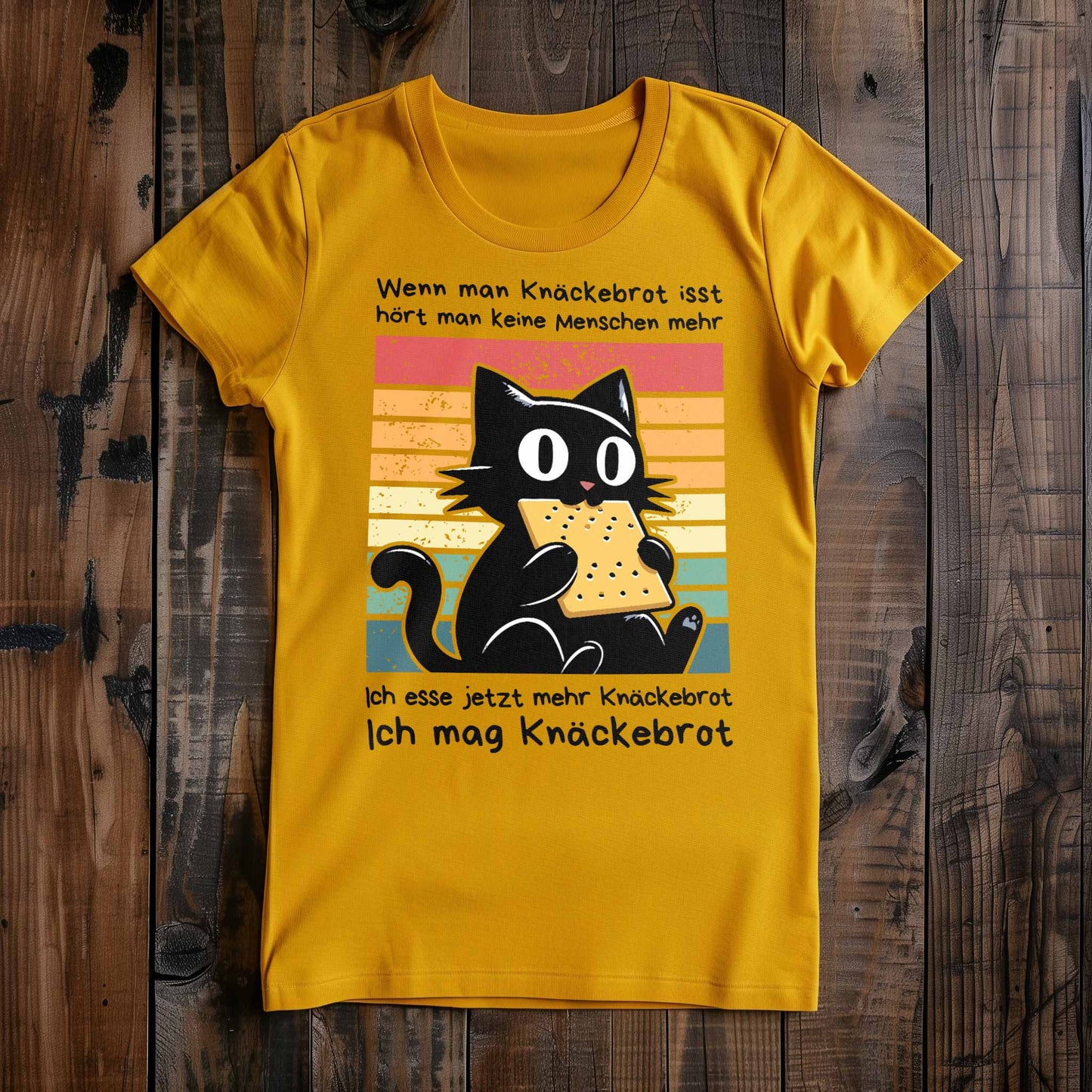 Gelbes Damen-Shirt auf Holzboden mit Design einer schwarzen Katze und dem Spruch 'Ich mag Knäckebrot'