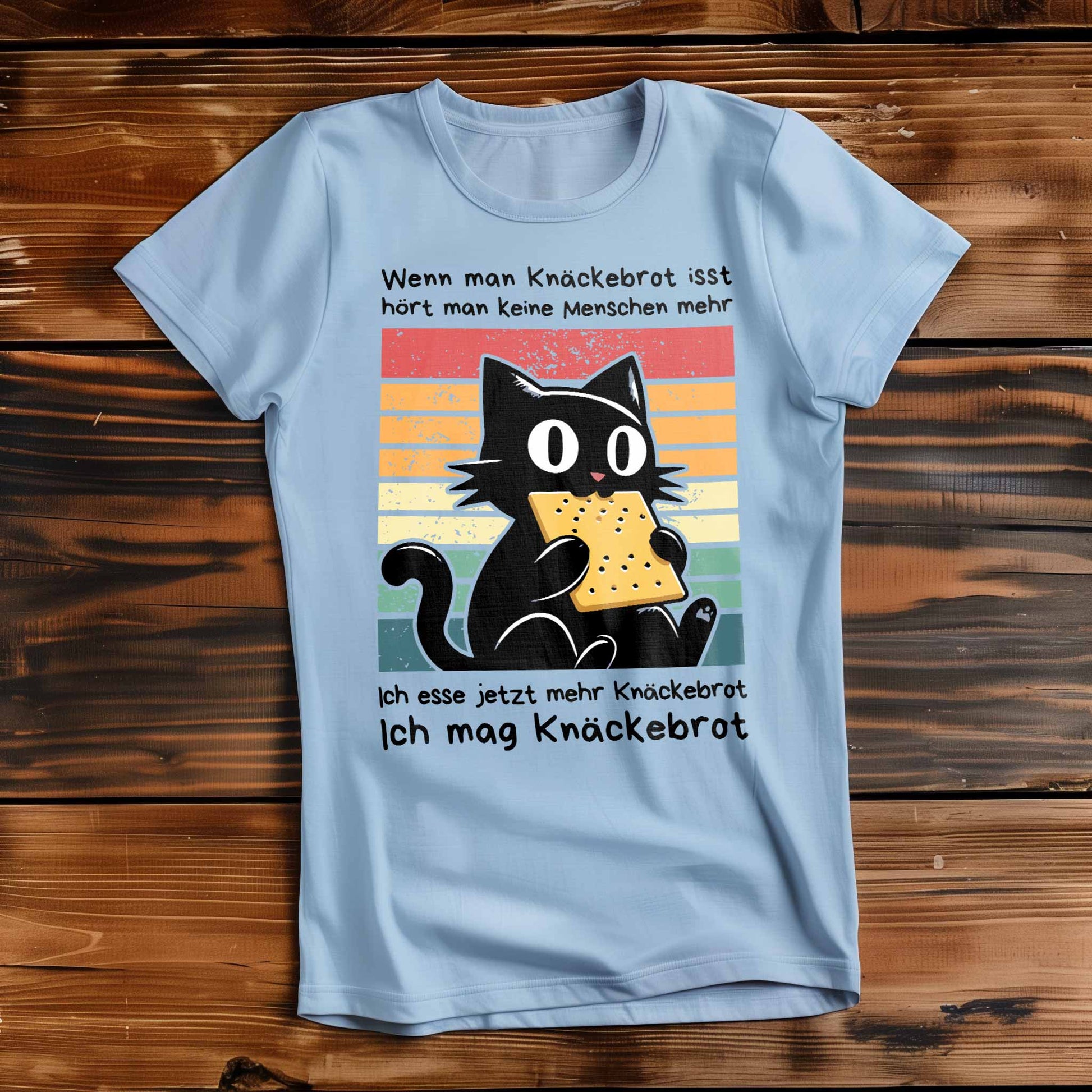 Himmel-Blaues Damen-Shirt auf Holzboden mit Design einer schwarzen Katze und dem Spruch 'Ich mag Knäckebrot'