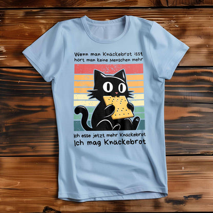 Himmel-Blaues Damen-Shirt auf Holzboden mit Design einer schwarzen Katze und dem Spruch 'Ich mag Knäckebrot'