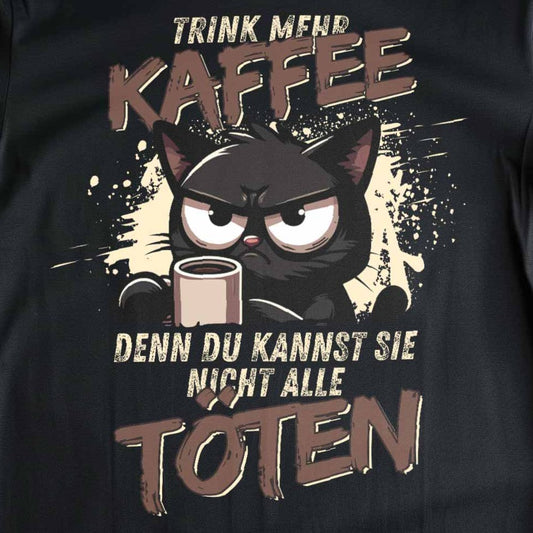 Nahaufnahme eines schwarzen T-Shirts mit Design einer Kaffee trinkenden Katze und dem lustigen Spruch 'Trink mehr Kaffee, denn Du kannst sie nicht alle töten'