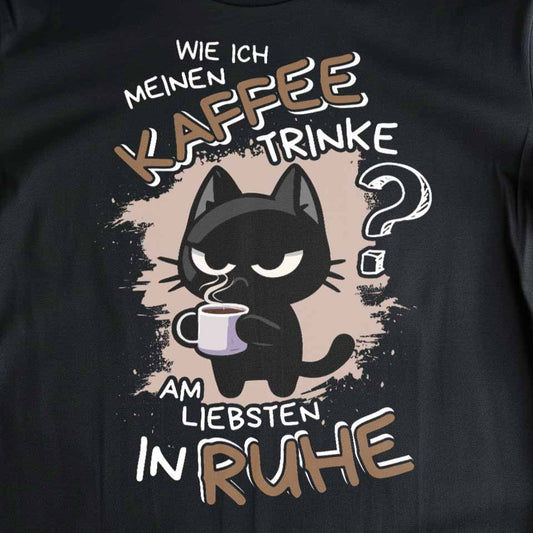 Nahaufnahme eines schwarzen T-Shirts mit Design einer süßen schwarzen Katze und dem lustigen Spruch 'Wie ich meinen Kaffee trinke? Am liebsten IN RUHE'