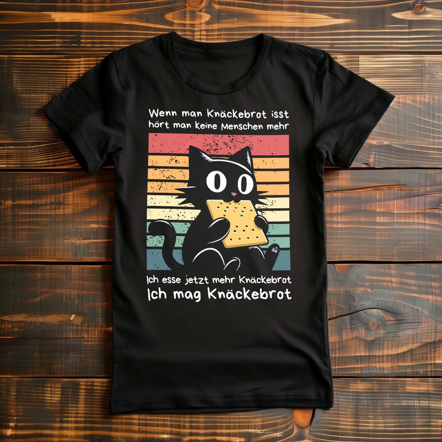 Schwarzes Damen-Shirt auf Holzboden mit Design einer schwarzen Katze und dem Spruch 'Ich mag Knäckebrot'