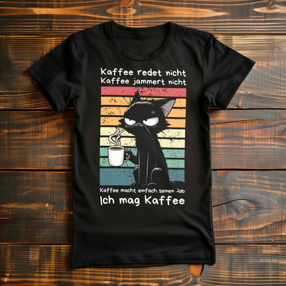 Schwarzes Damen-Shirt auf Holzboden mit Kaffee trinkender Katze und dem lustigen Spruch 'Ich mag Kaffee'