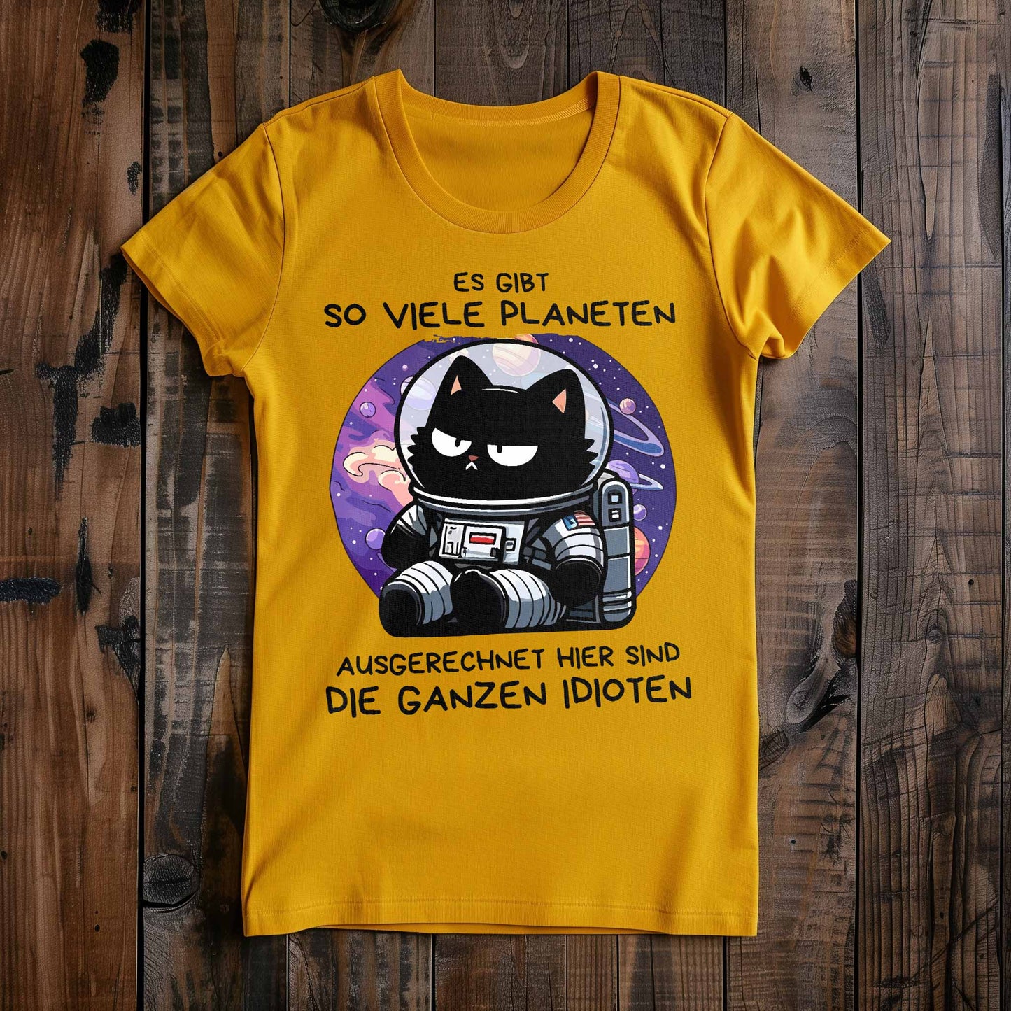 Gelbes Damen-Shirt auf Holzboden mit Design einer Astronauten-Katze im Weltraum und dem lustigen Spruch 'Es gibt so viele Planeten, ausgerechnet hier sind die ganzen Idioten'