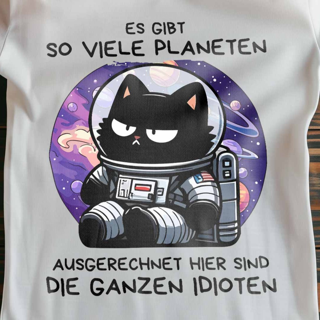 Nahaufnahme eines weißen Damen-Shirts auf Holzboden mit Design einer Astronauten-Katze im Weltraum und dem lustigen Spruch 'Es gibt so viele Planeten, ausgerechnet hier sind die ganzen Idioten'