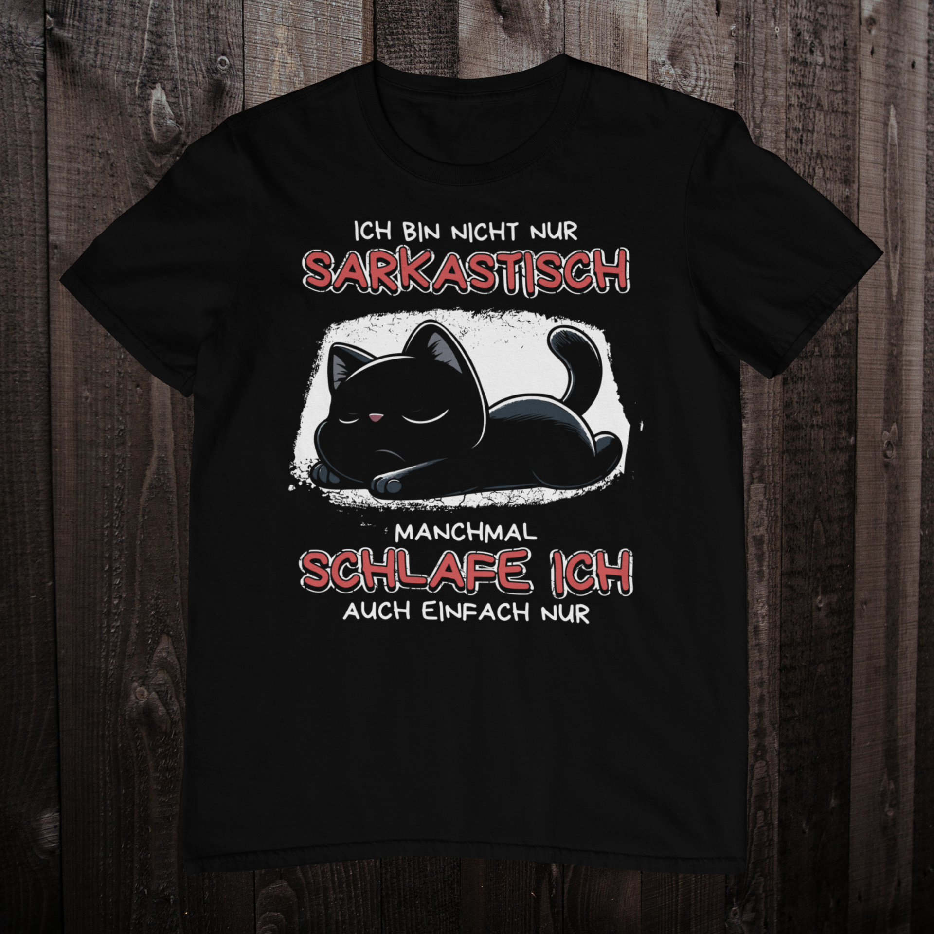 Schwarzes T-Shirt auf einem dunklen Holzboden mit einem Design einer schlafenden Katze und dem lustigen Spruch 'Ich bin nicht nur sarkastisch - Manchmal schlafe ich auch einfach nur'