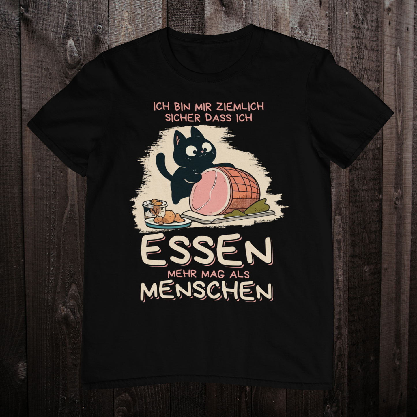 Schwarzes T-Shirt auf einem Holzboden zeigt ein Design einer schwarzen Katze mit einem Schweinebraten und dem lustigen Spruch: 'Ich bin mir ziemlich sicher, dass ich Essen mehr mag als Menschen'