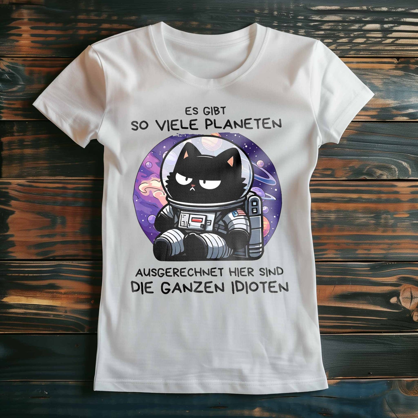 Weißes Damen-Shirt auf Holzboden mit Design einer Astronauten-Katze im Weltraum und dem lustigen Spruch 'Es gibt so viele Planeten, ausgerechnet hier sind die ganzen Idioten'