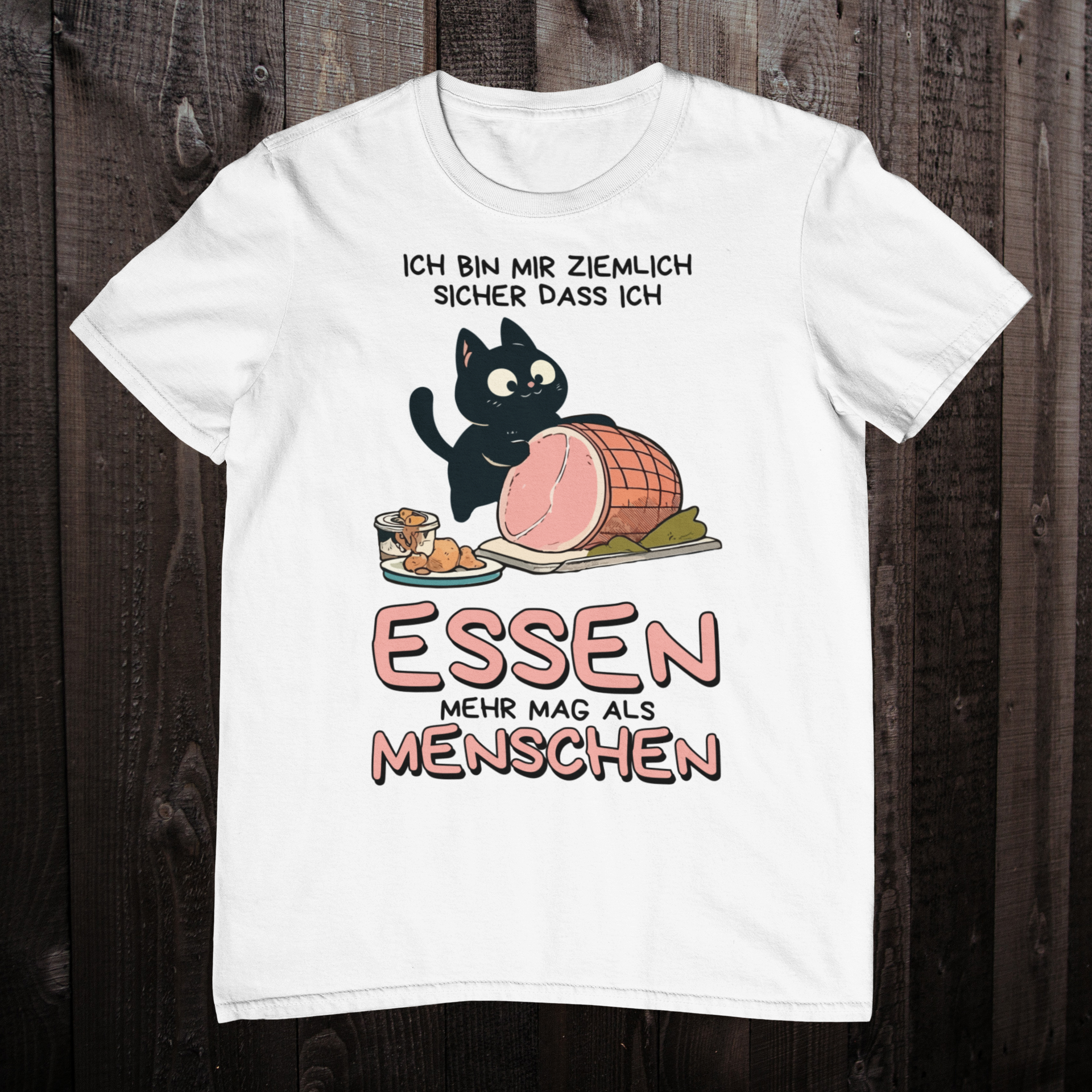 Weißes T-Shirt auf einem Holzboden zeigt ein Design einer schwarzen Katze mit einem Schweinebraten und dem lustigen Spruch: 'Ich bin mir ziemlich sicher, dass ich Essen mehr mag als Menschen'