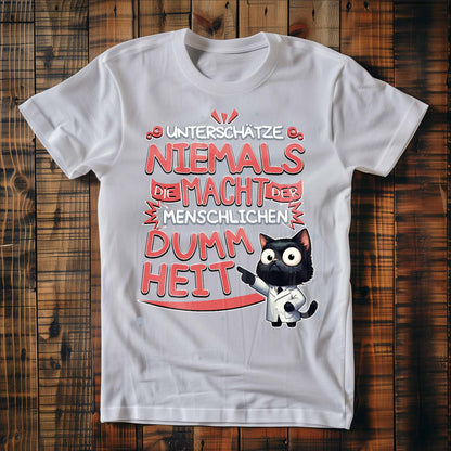 Weißes T-Shirt auf Holzboden mit Design einer Katze als Doktor mit dem lustigen Spruch 'Unterschätze niemals die Macht der menschlichen Dummheit'